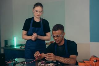 Formatrice accompagnant un jeune en lunettes de protection sur un poste de montage électronique