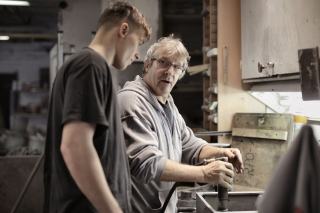 Compagnon expérimenté montrant un geste technique à un apprenti dans l'atelier