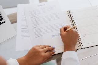 Mains signant un contrat posé sur un bureau, carnet et stylos à côté