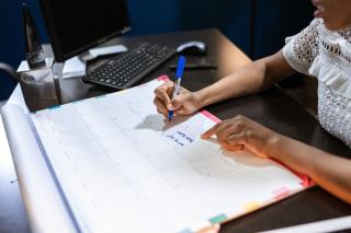 Personne notant des dates sur un grand planning mensuel posé sur un bureau