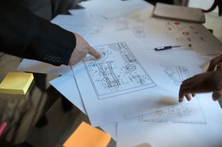 Mains désignant des plans de pièces mécaniques étalés sur une table