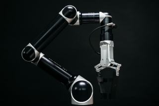 Bras robotique collaboratif noir et blanc muni d'une pince, sur fond noir