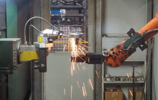 Robot industriel orange réalisant une opération dans une gerbe d'étincelles