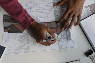 Mains traçant un plan technique à l'équerre sur une table de travail