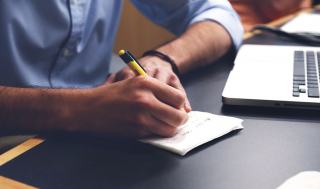 Main rédigeant une lettre au stylo à côté d'un ordinateur portable